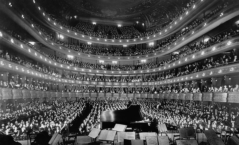 Historic opera house during a live opera performance with orchestra and singers on stage.