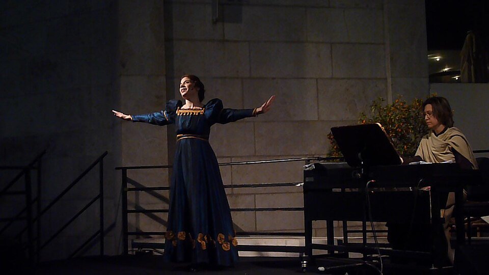 Opera singer performing with an orchestra during a live performance.